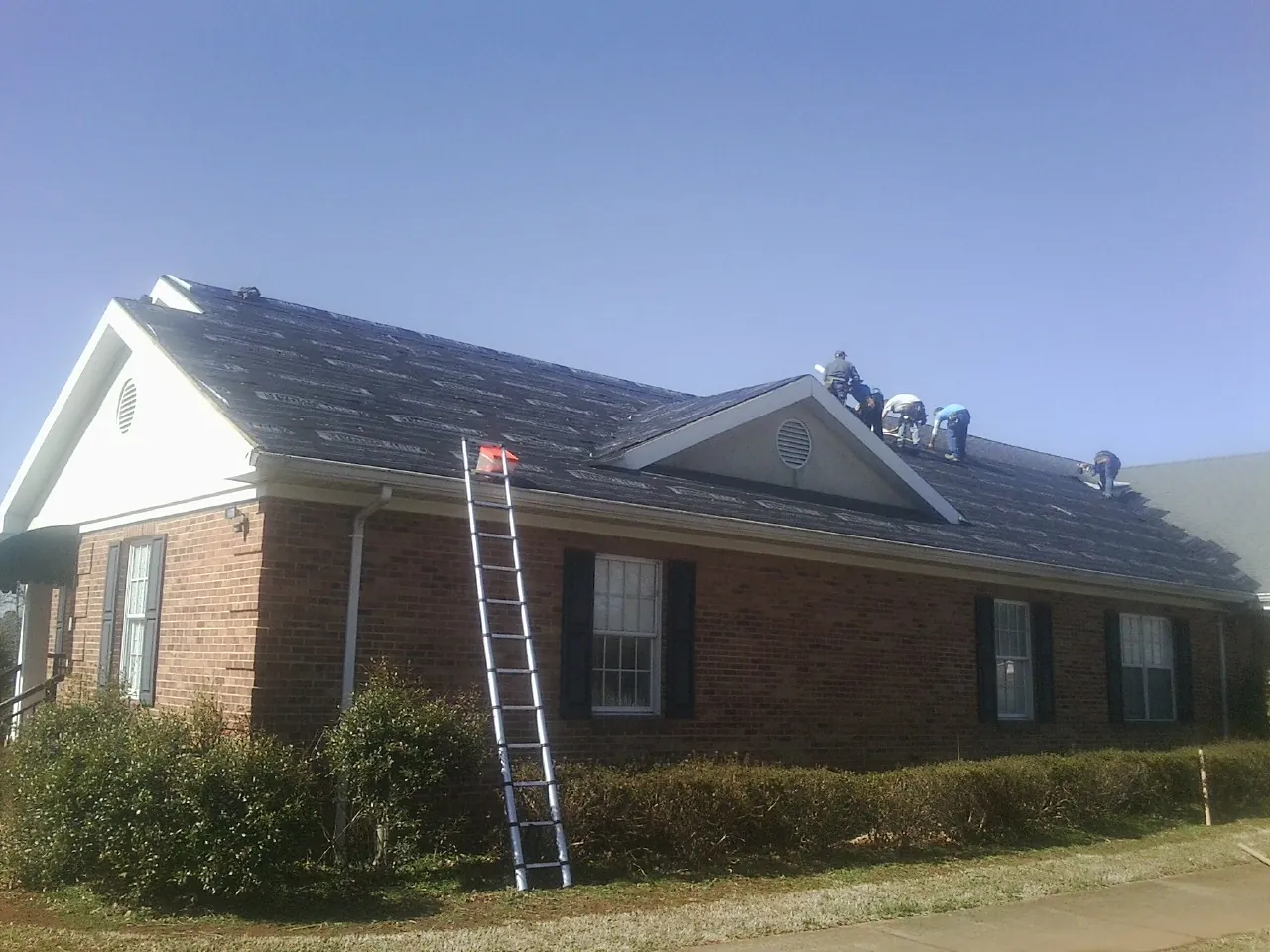 Crew tearing shingles off a brick ranch roof with a ladder set — Emergency Roof Repair work by our crew in Northridge