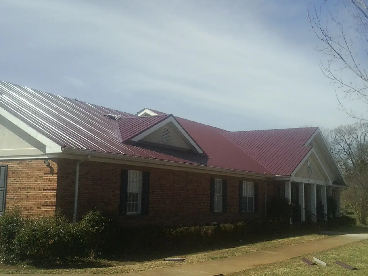 Red metal roof with gabled entries on a long brick building, from a Hail Damage Roof Repair job in Northridge