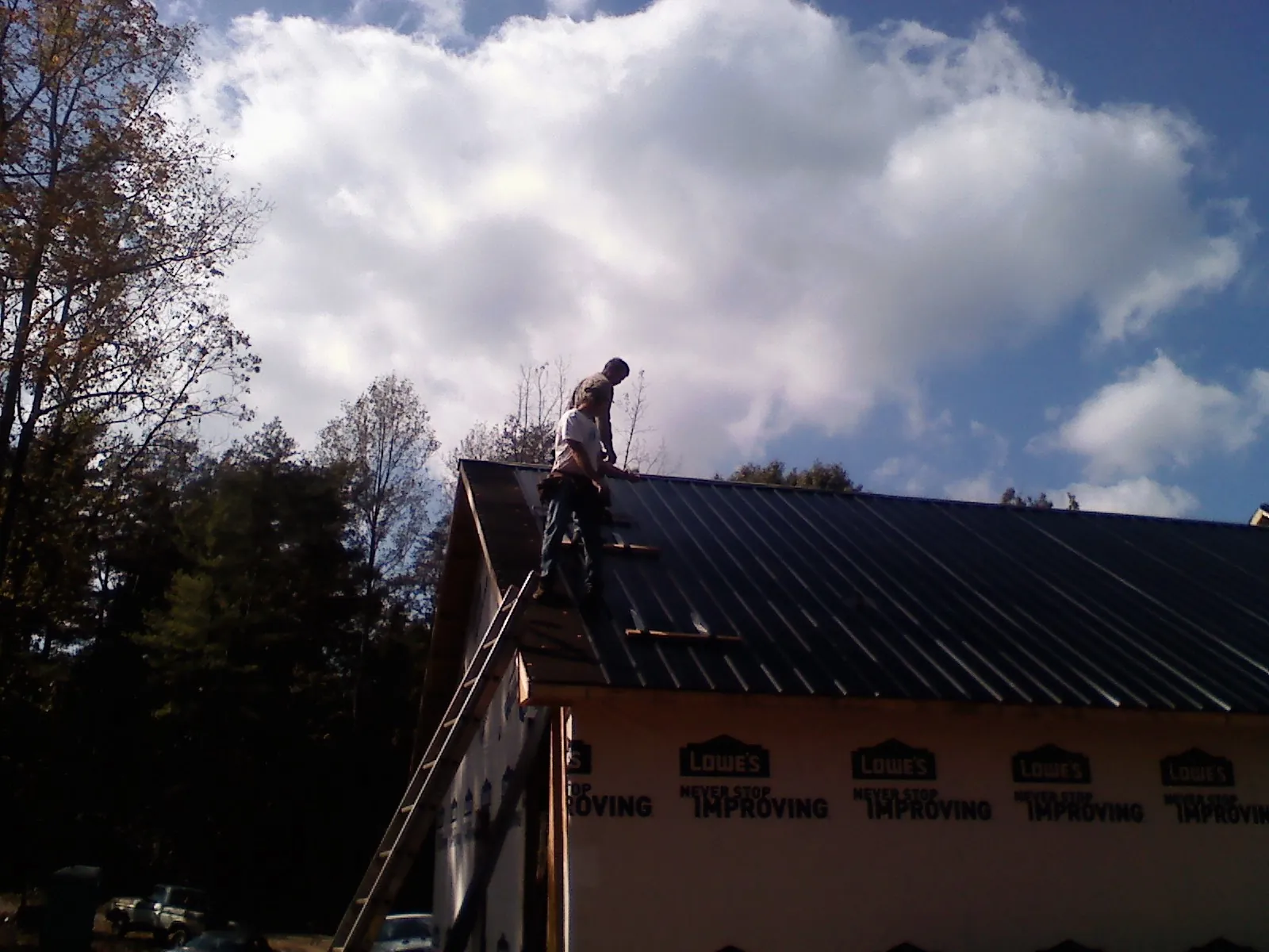 Roofer fastening dark metal panels high against a cloudy sky, from a Roof Inspection job in Northridge