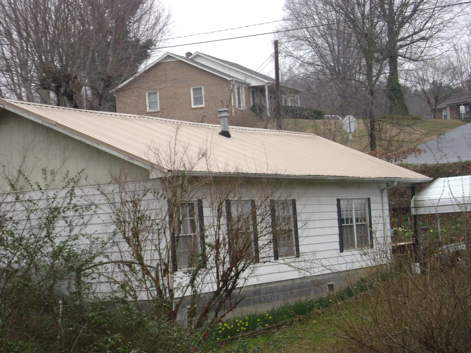 Tan metal roof on a white sided house set into a hillside — Commercial Roofing by Roofing Brothers in Northridge